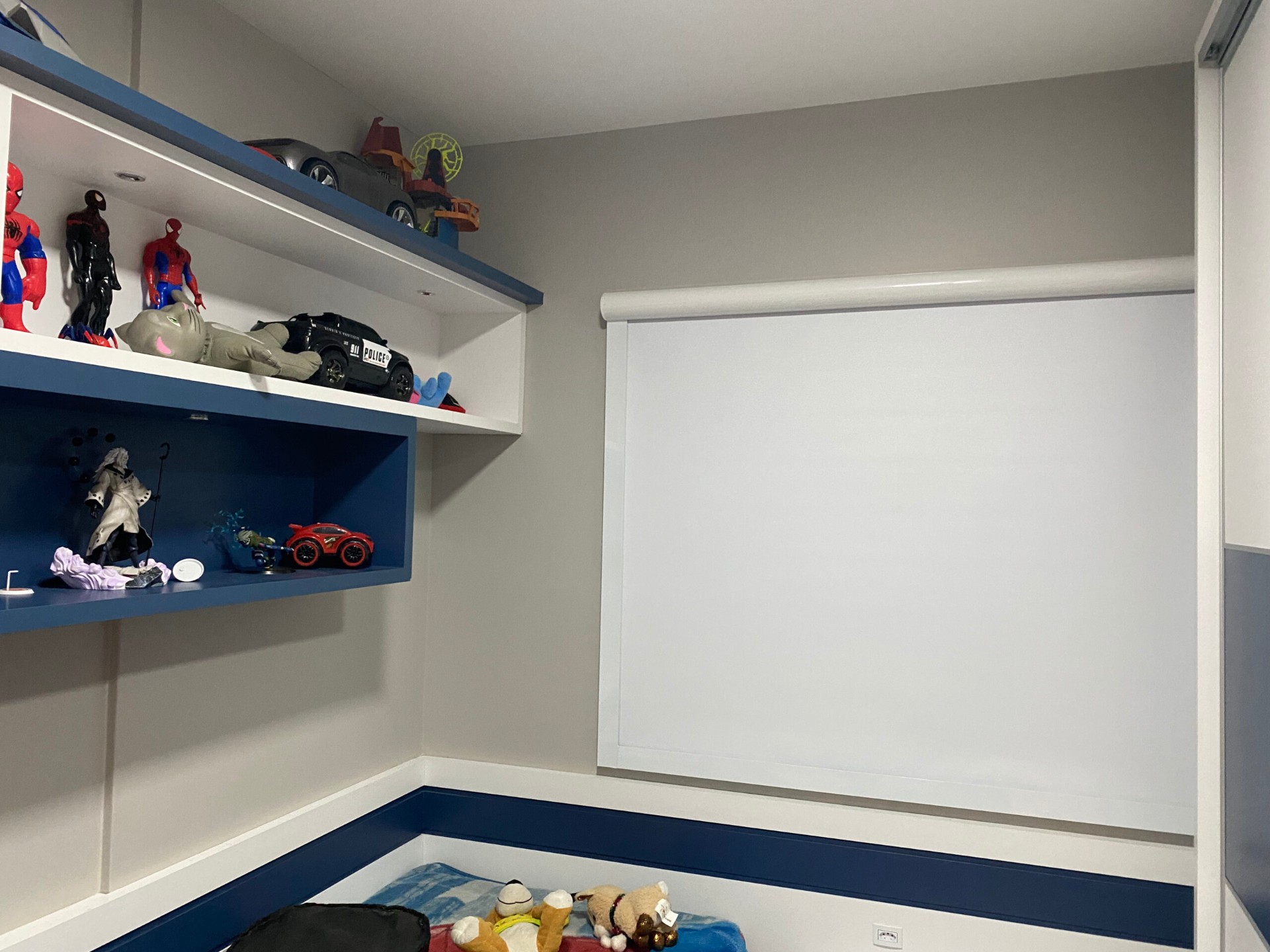 Cortina rolô clara em quarto com prateleiras e brinquedos.