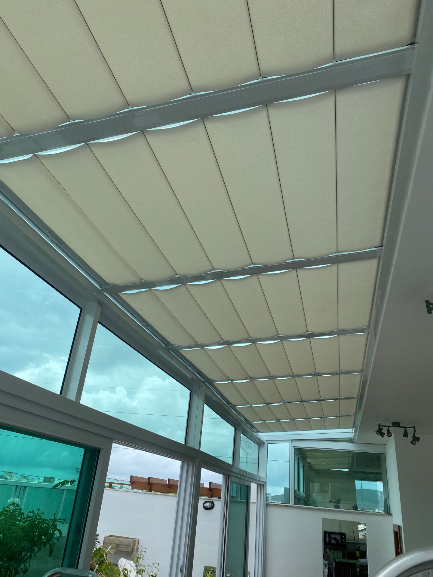 Cortinas claras acompanhando a estrutura de um teto de vidro.