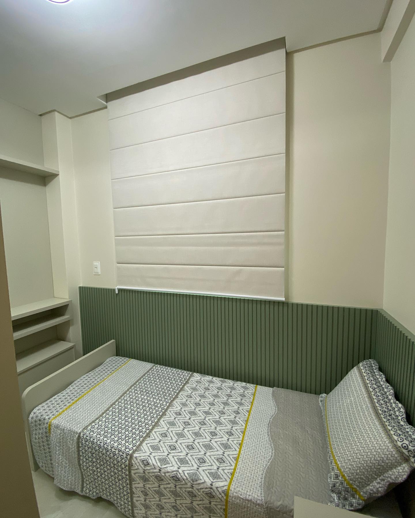Cortina romana clara acima da cama, em quarto com parede verde.